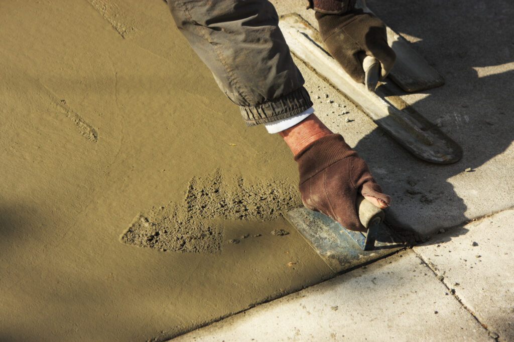 Concrete mason smooths freshly poured concrete sidewalk using trowel masonry tool.  San Francisco, California, 2009.